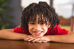 Unaltered Prints: Portrait of happy hispanic boy with curly black hair leaning on table at home