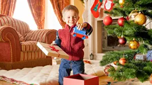 Unpacking Prints: Portrait of happy smiling little boy taking out toy train from Christmas gift box