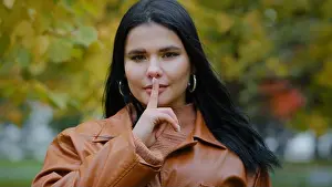 Gossip Prints: Portrait hispanic woman stands outdoors serious girl looking at camera holds index finger near mouth forbids speaking
