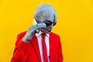 Mid Adults Prints: Portrait of man wearing alien costume and bright red suit using smart phone