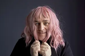 Comical Prints: Portrait of a man who tried on a pink wig, looks at the camera, grimaces, poses. Close-up