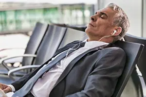 Formal Wear Prints: Portrait of mature businessman listening to music on his smartphone while sleeping and waiting for boarding in airport