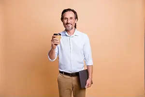 Pause Prints: Portrait of nice cheerful man holding in hands laptop drinking take out latte isolated over beige pastel color