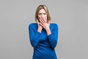 Shocked Prints: Portrait of scared young woman in elegant tight blue dress covering her mouth with hands
