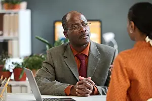 Assist Prints: Portrait of senior African American businessman listening to young colleague in office with serious face expression