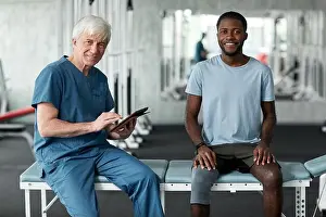 Assist Prints: Portrait of senior rehabilitation therapist smiling at camera while consulting young man in clinic