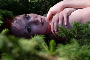 Redhead Prints: portrait of sexy young naked redhead blue eyed woman lying on forest floor between small spruce trees whose branches