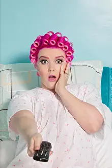 Remote Control Prints: Portrait of shocked woman holding remote with hair curlers sitting on bed