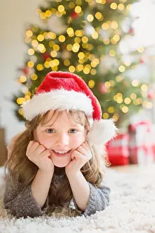 Caiaalamy Prints: Portrait smiling girl wearing Santa hat on rug in living room with Christmas tree