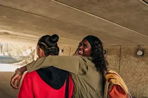 Leisure Time Prints: Portrait of smiling woman with arm around male friend walking together in underpass