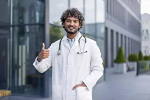 Dentist Prints: Portrait of a smiling young male doctor standing outside the hospital in a white coat