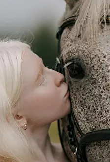 Horsewoman Prints: Portrait of young albino woman standing near gray horse and kisses it on meadow