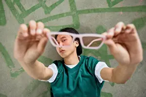 Eyeglasses Prints: Portrait of young Asian man wearing colorful casual wear holding sunglasses to camera
