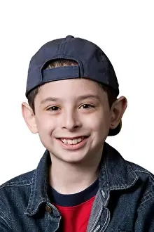 Portrait of a young Caucasian boy wearing a backwards facing baseball cap on a white background