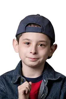 Portrait of a young Caucasian boy wearing a backwards facing baseball cap on a white background