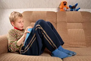 Concentrating Prints: portrait of a young fair haired boy lying on a sofa and reading a book