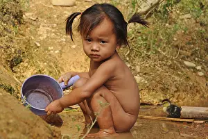 Portrait of a young girl in Laos playing in the mud