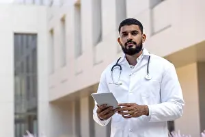 Gynecology Prints: Portrait of a serious young male doctor standing with a tablet in his hands near the clinic