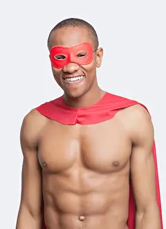 Superhero Prints: Portrait of young shirtless man in superhero costume smiling gainst gray background