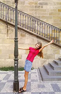 Outstretched Prints: Portrait of a Young woman holding a lamp post smiling