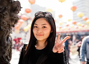 Chinese Ethnicity Prints: Portrait of young woman with long hair and sunglasses on head doing peace sign