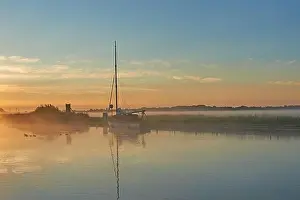 Potter Heigham, Norfolk Broads and a sailing boat moored on the River Thurne during a misty summer sunrise