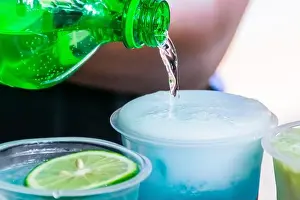 Pouring a soda water into a transparent plastic glass with cold shaved ice inside
