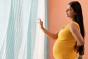 Abdomen Prints: Pregnant woman looking out of window at home with holding her back