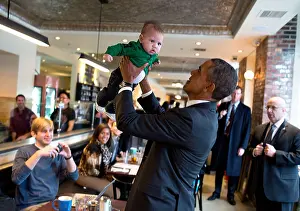 Playing Prints: US President Barack Obama lifts a baby while greeting patrons prior to lunch at The Coupe restaurant January 10