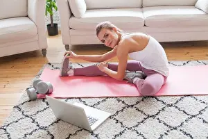 Dumbbell Prints: Pretty fit woman wearing sportswear doing fitness stretching exercises and using laptop at home