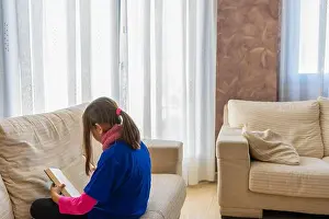 Cushion Prints: Pretty girl in a black tights and blue blouse reading a book on the white sofa in her living room