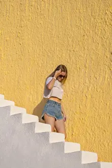 Ladder Prints: Pretty girl comes down stairs. Blonde woman with long hair walks up white staircase against backdrop of yellow house