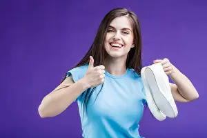 Trainers Prints: Pretty happy smiling brunette girl dressed in blue t-shirt holding sport footwear sneakers before blue background