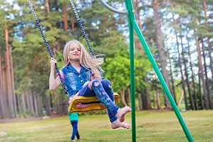 Pretty little blonde girl swinging outdoors on playground