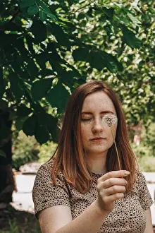 Redhead Prints: Pretty redhead girl with freckles holding a dandelion and covering her one eye with it in the park