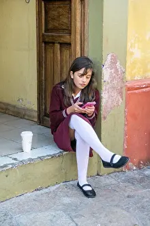 pretty teenage schoolgirl sits on stoop in school uniform with spotless white stockings using her cellphone San Cristobal