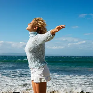 Maui Prints: Pretty young blond woman standing on Maui Hawaii beach with arms out to side and wind blowing hair smiling