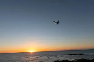 Hovering Prints: Professional Drone flying at Sunrise over the sea. The sky is glowing