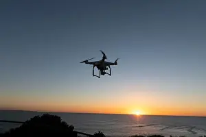 Hovering Prints: Professional Drone flying at Sunrise over the sea. The sky is glowing