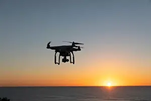 Professional Drone flying at Sunrise over the sea. The sky is glowing