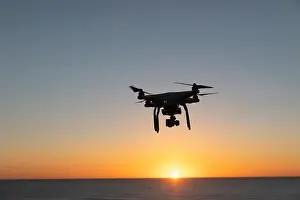 Hovering Prints: Professional Drone flying at Sunrise over the sea. The sky is glowing