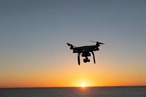 Hovering Prints: Professional Drone flying at Sunrise over the sea. The sky is glowing