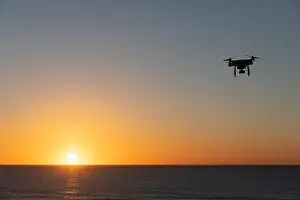 Hovering Prints: Professional Drone flying at Sunrise over the sea. The sky is glowing