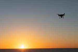 Professional Drone flying at Sunrise over the sea. The sky is glowing