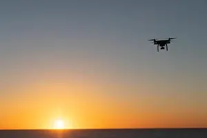 Professional Drone flying at Sunrise over the sea. The sky is glowing