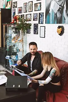 Discuss Prints: Professional tattoo master sitting on sofa with girl discussing sketch of new tattoo spending time in studio