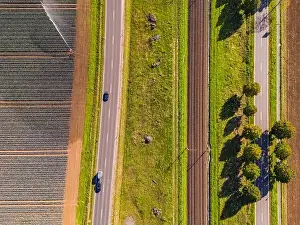 A railroad line with two tracks next to two roads and fields next to agricultural fields