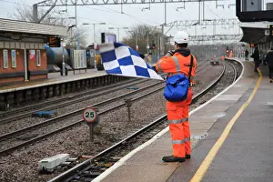 Checked Prints: Railway worker wearing high visibility orange clothing holds blue and white checkered safety flag