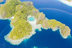 A rainbow appears above a rugged limestone island in Raja Ampat, Indonesia. This remote, tropical region is known for its marine biodiversity