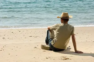 Contemplating Prints: Rare view of a young man wearing cowboy hat sitting on the beach